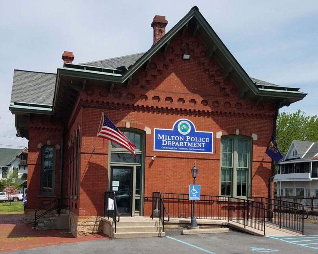 Historic red brick building housing the Milton Police Department in Milton, Pennsylvania, with accessible entrance and American flag